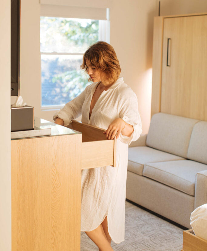 Woman in a white robe standing in a modern living room with a couch and window.
