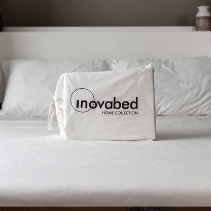White sheet set with white pillowcases with Inovabed Home Collection - Queen Sheet Set packaging sitting on top of the bed.