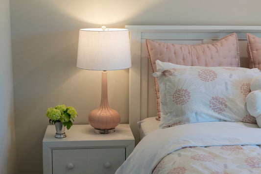 simple bedroom with a pink and white bed and a pink lamp on a small bedside table