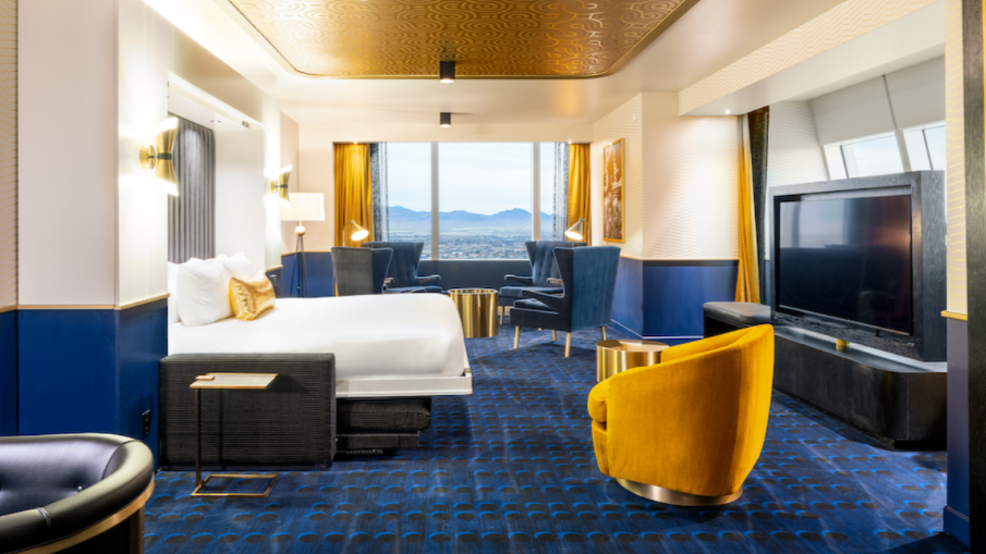 Circa hotel room with blue and gold decor, including a bed, chair, and TV. Murphy bed