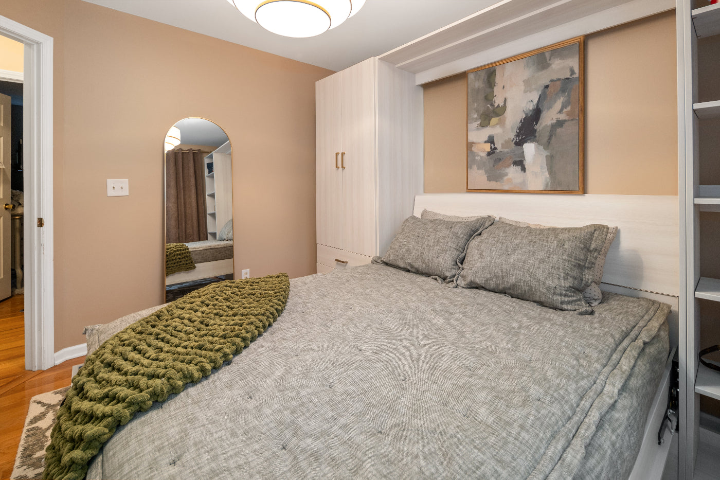 Bedroom with a bed, green blanket, and abstract painting on the wall.
